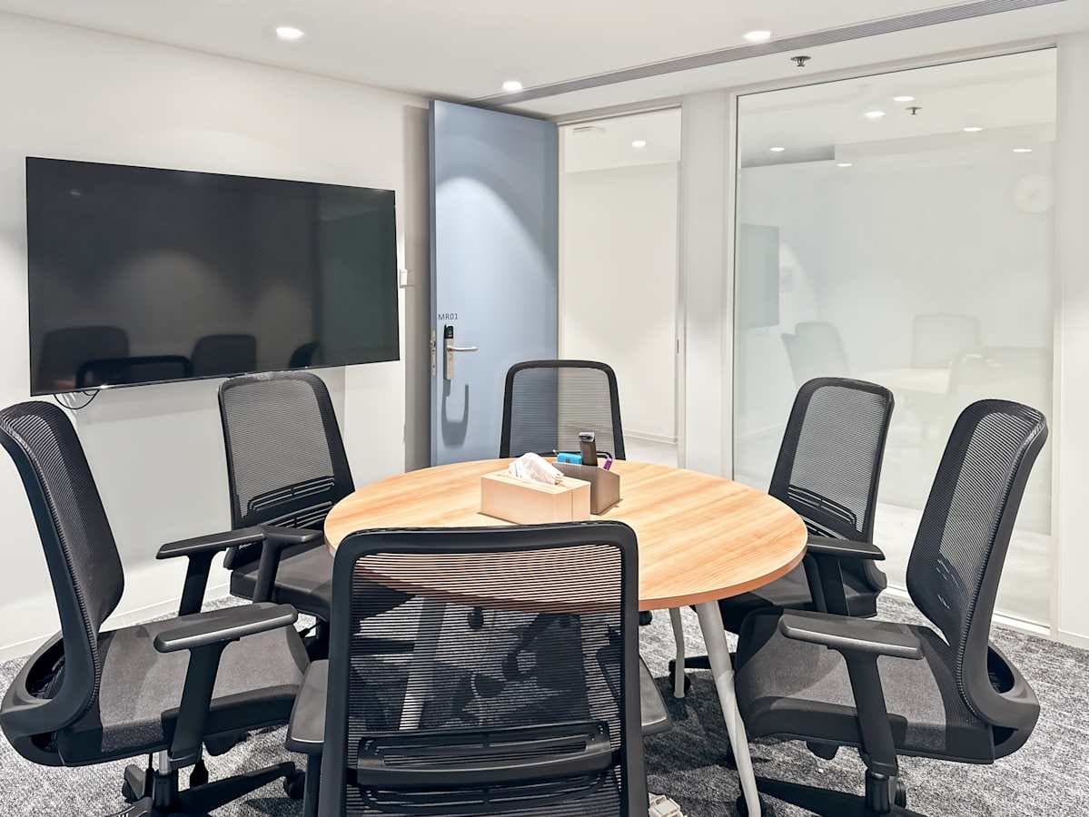Modern meeting room with sleek chairs and a round table, featuring a large screen and ample lighting.