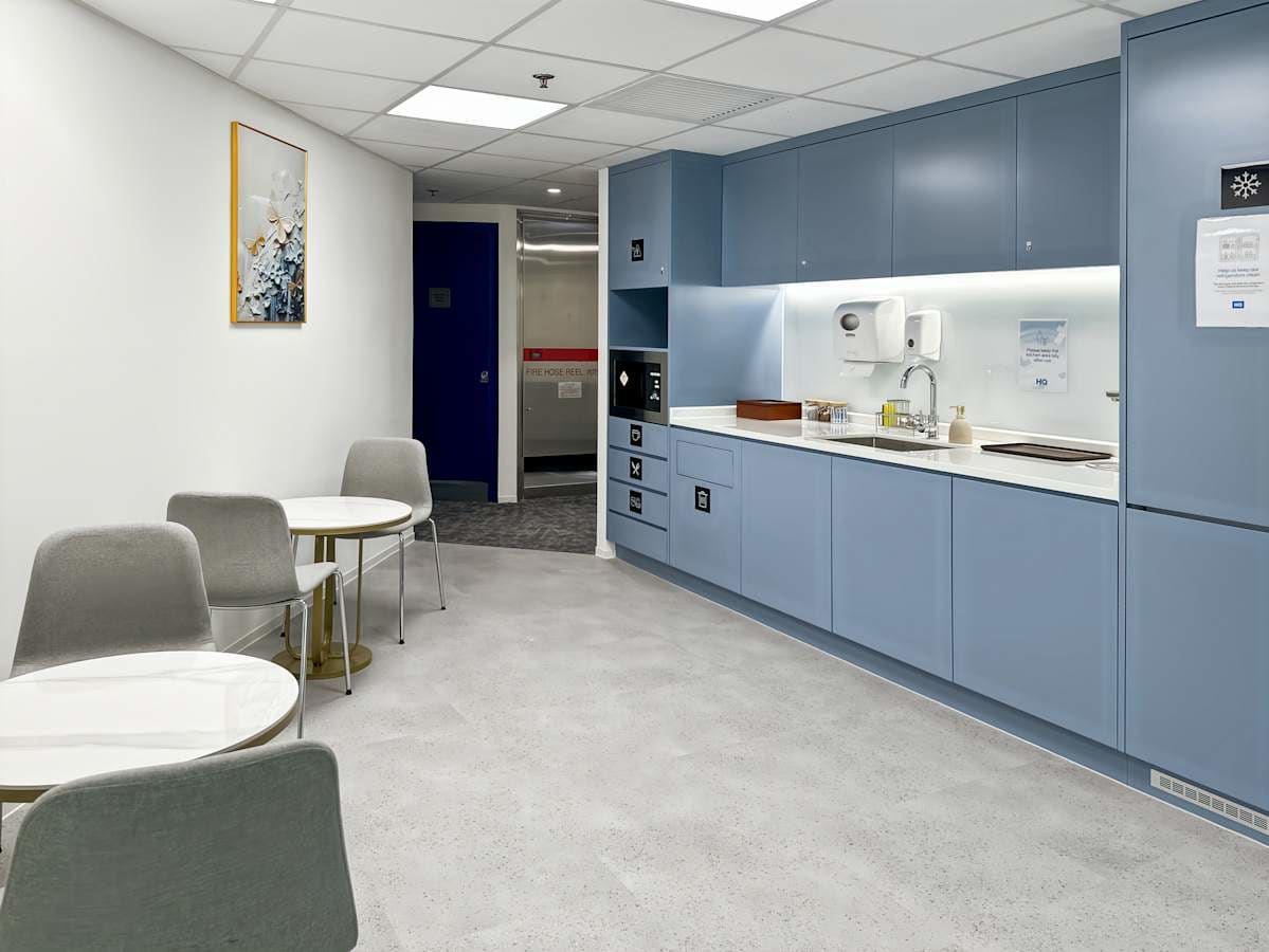 Modern kitchenette in a flexible coworking space, featuring sleek blue cabinets and cozy seating.