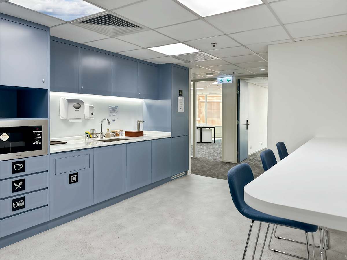 Modern kitchenette with blue cabinetry, ample seating, and sleek lighting in a coworking space.