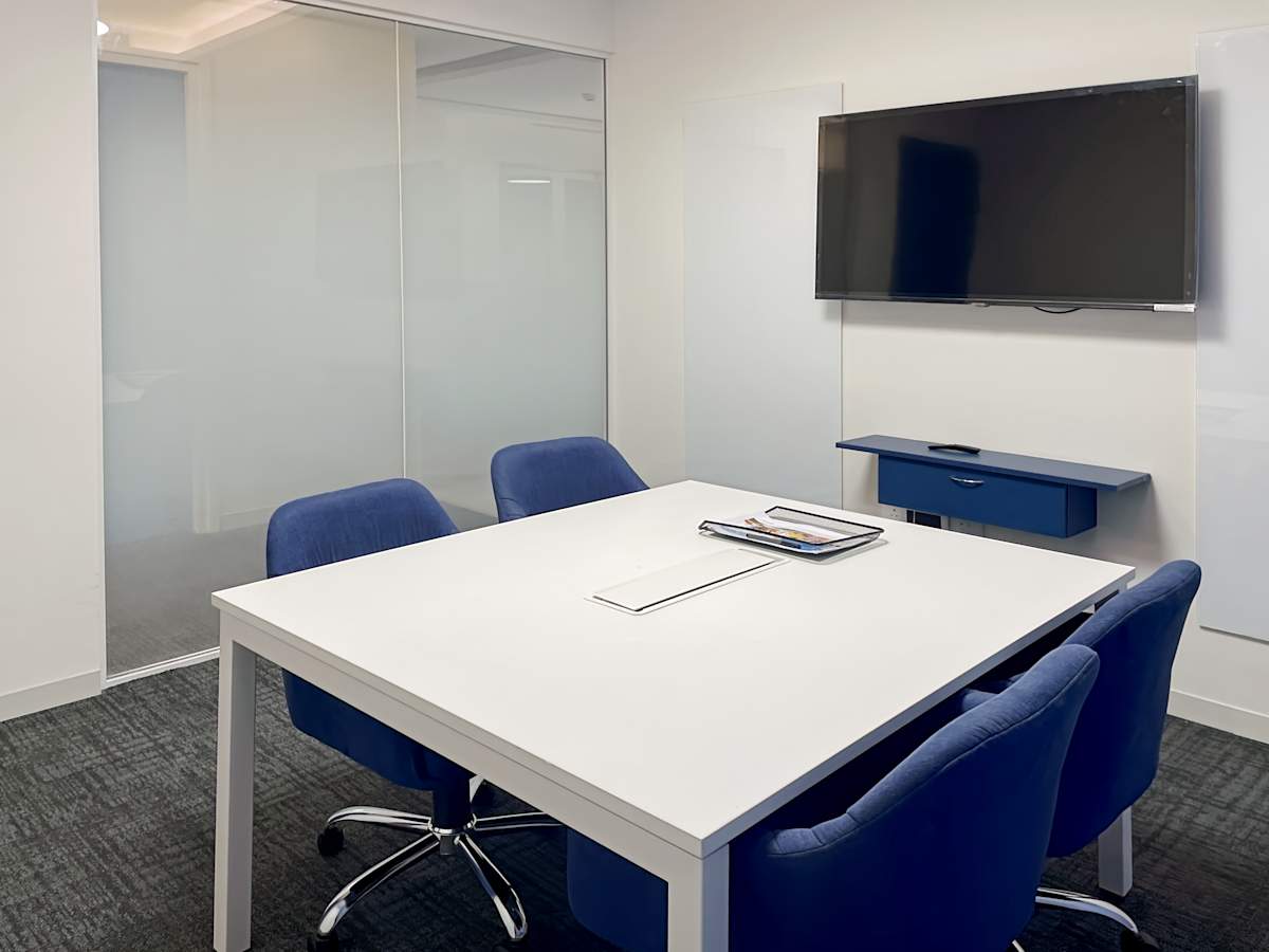Modern meeting room with a sleek table, plush blue chairs, and a wall-mounted screen.