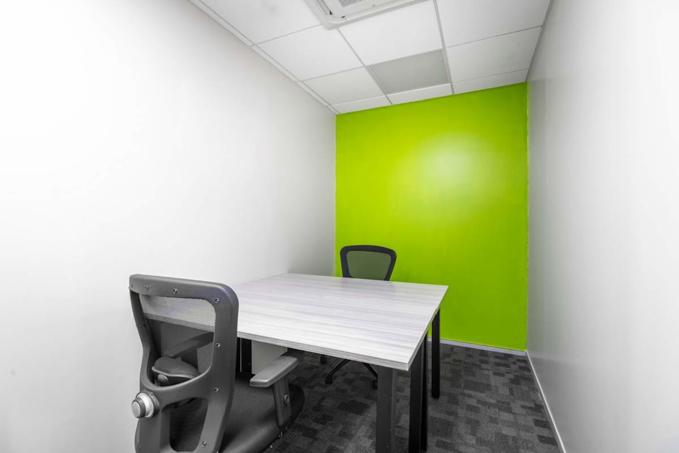 Compact coworking space with vibrant green accent wall and modern seating. Ideal for focused work.