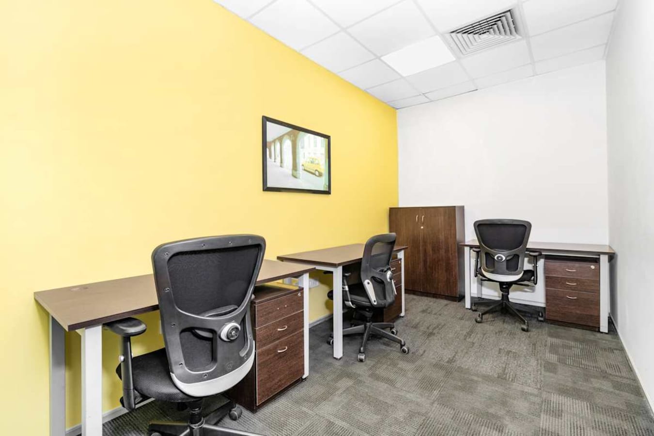 Modern coworking space with ergonomic chairs, bright yellow accent wall, and ample storage.