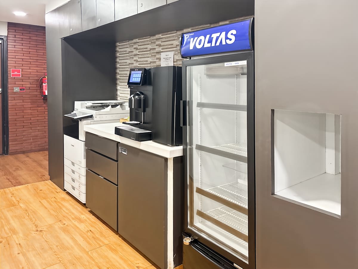 Modern pantry with fridge, coffee machine, and ample storage space in a flexible coworking area.