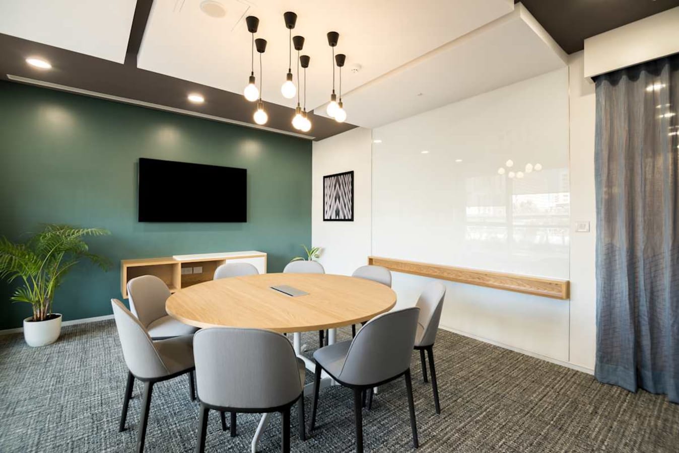 Modern coworking room with a round table, seating for six, and a whiteboard, under stylish lighting.