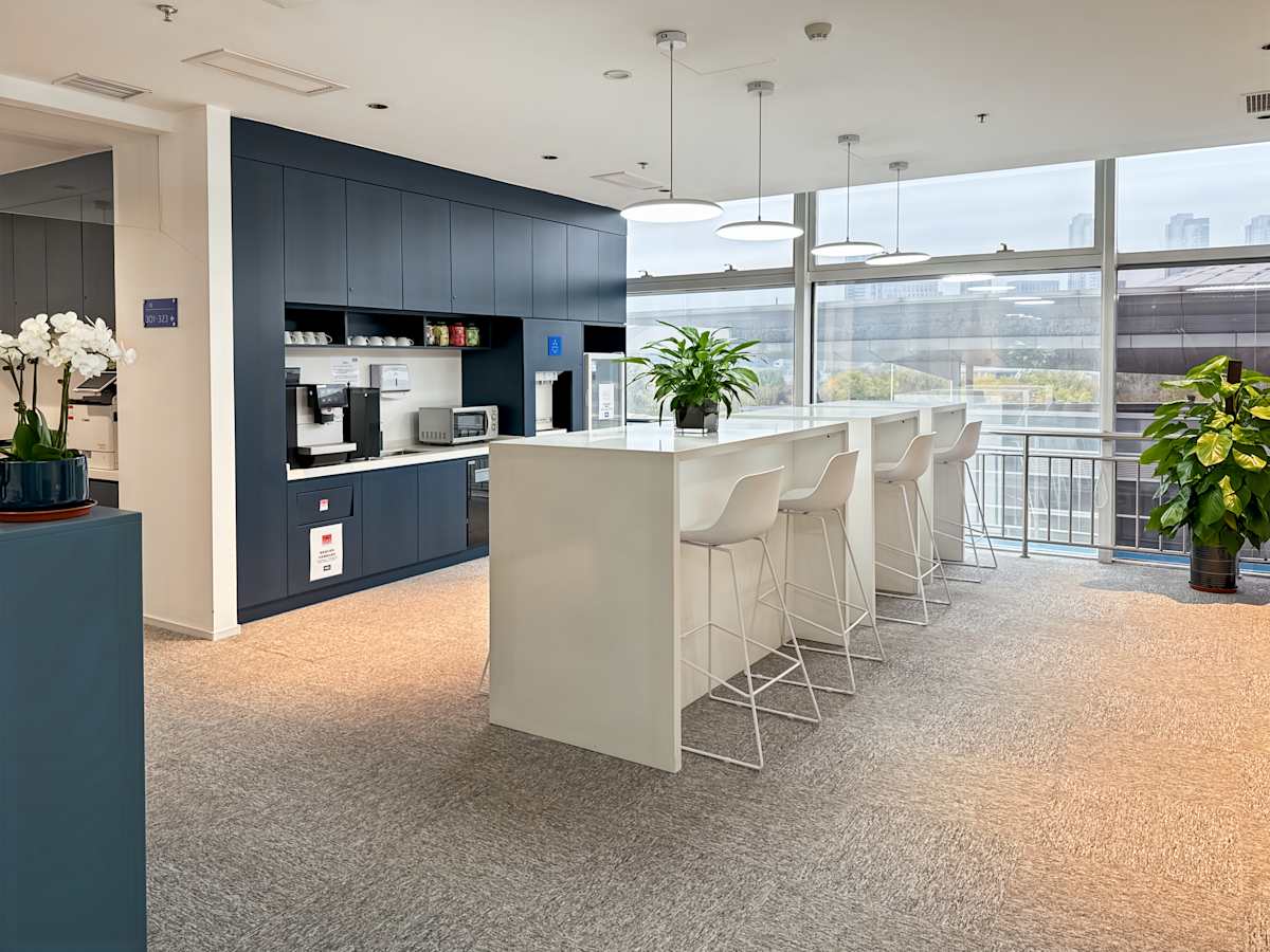 Modern coworking space with sleek kitchen, ample seating, and natural light. Ideal for collaboration.
