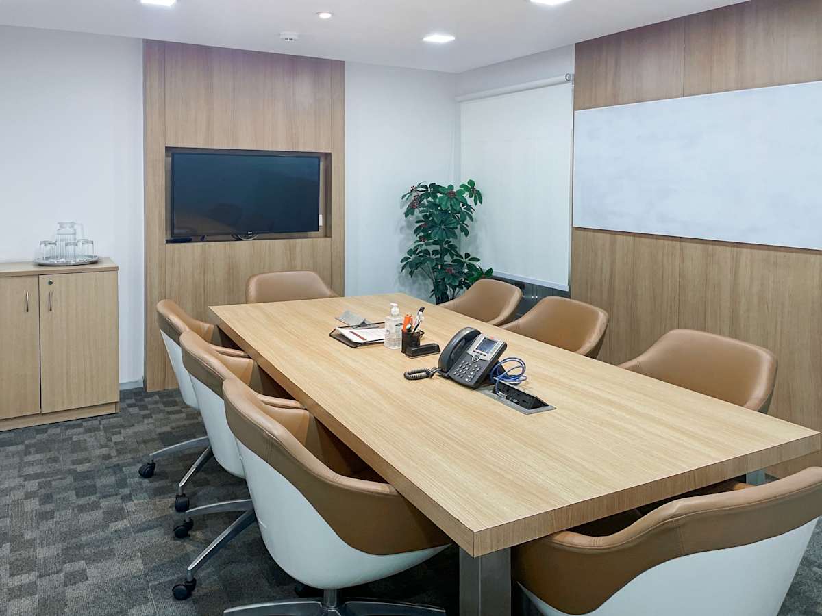 Modern conference room with sleek wood table, ergonomic chairs, and wall-mounted screen.