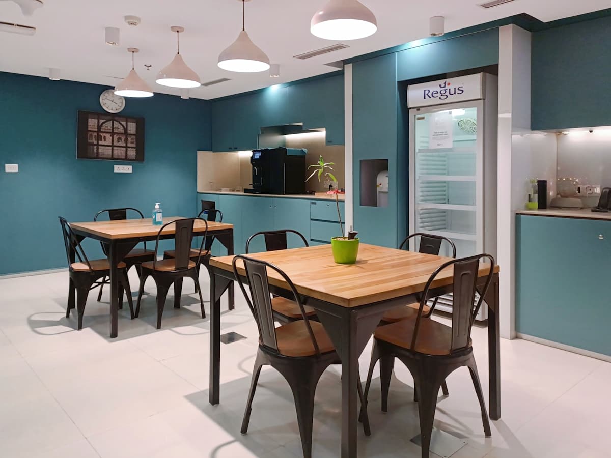 Modern coworking area with stylish lighting, wooden tables, and a well-equipped kitchenette.