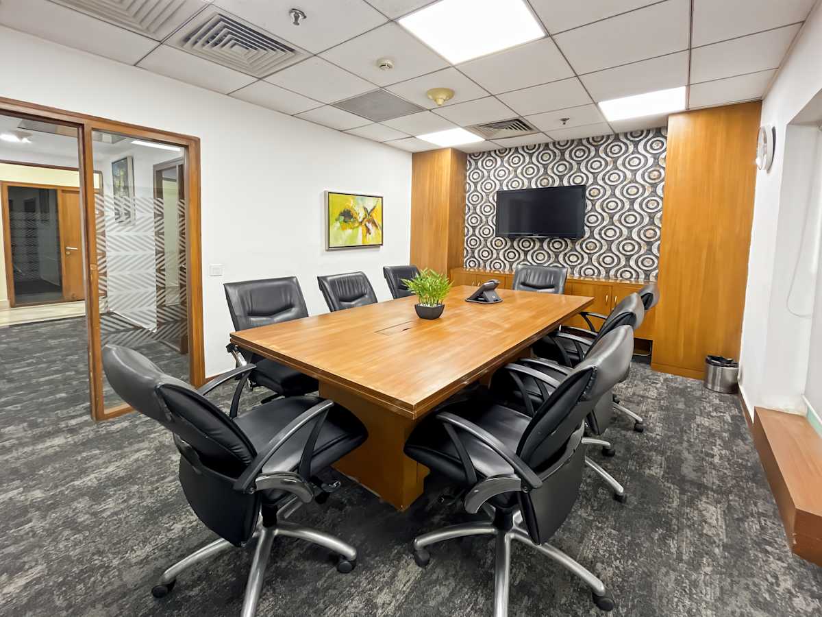 Modern meeting room with a large wooden table, ergonomic chairs, and a wall-mounted TV. Ideal for collaboration.