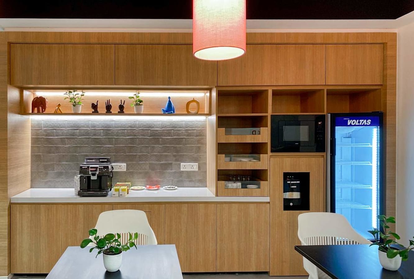Modern kitchenette with coffee machine, microwave, and ample shelving in a Turbhe coworking space.