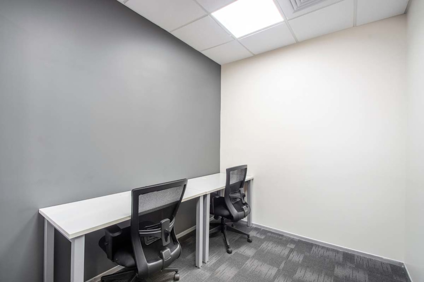 Modern coworking space with two ergonomic chairs, sleek desks, and ample lighting on Nallurhalli Road.
