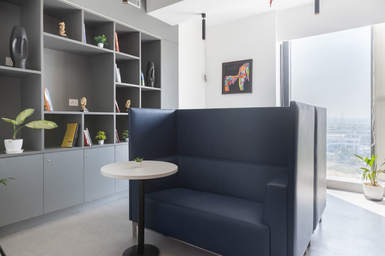 Modern coworking space with cozy seating, natural light, and stylish shelving in Delhi's Phase 1.