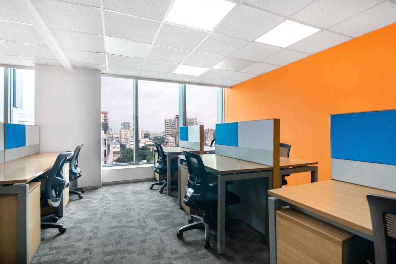 Bright coworking area with city views, ergonomic chairs, and vibrant accent wall. Ideal for collaboration.