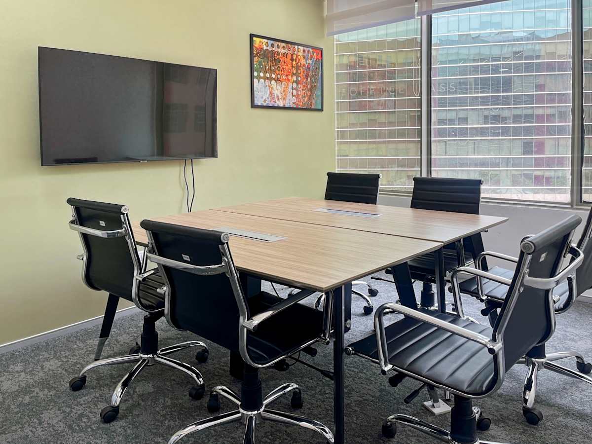 Modern meeting room with a large table, ergonomic chairs, and a wall-mounted screen. Ample natural light.