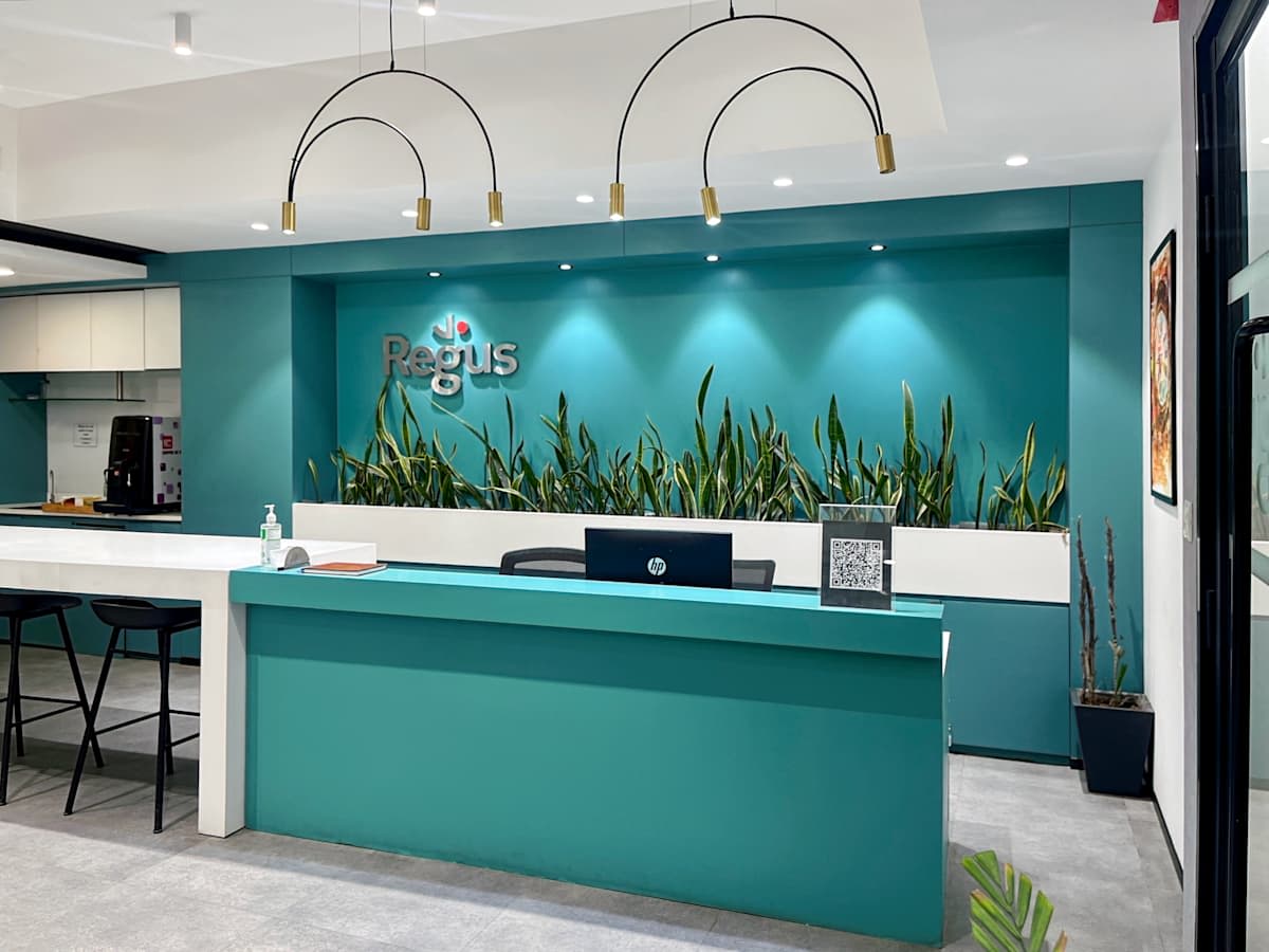 Modern coworking reception with vibrant teal accents and lush greenery in Gurugram.