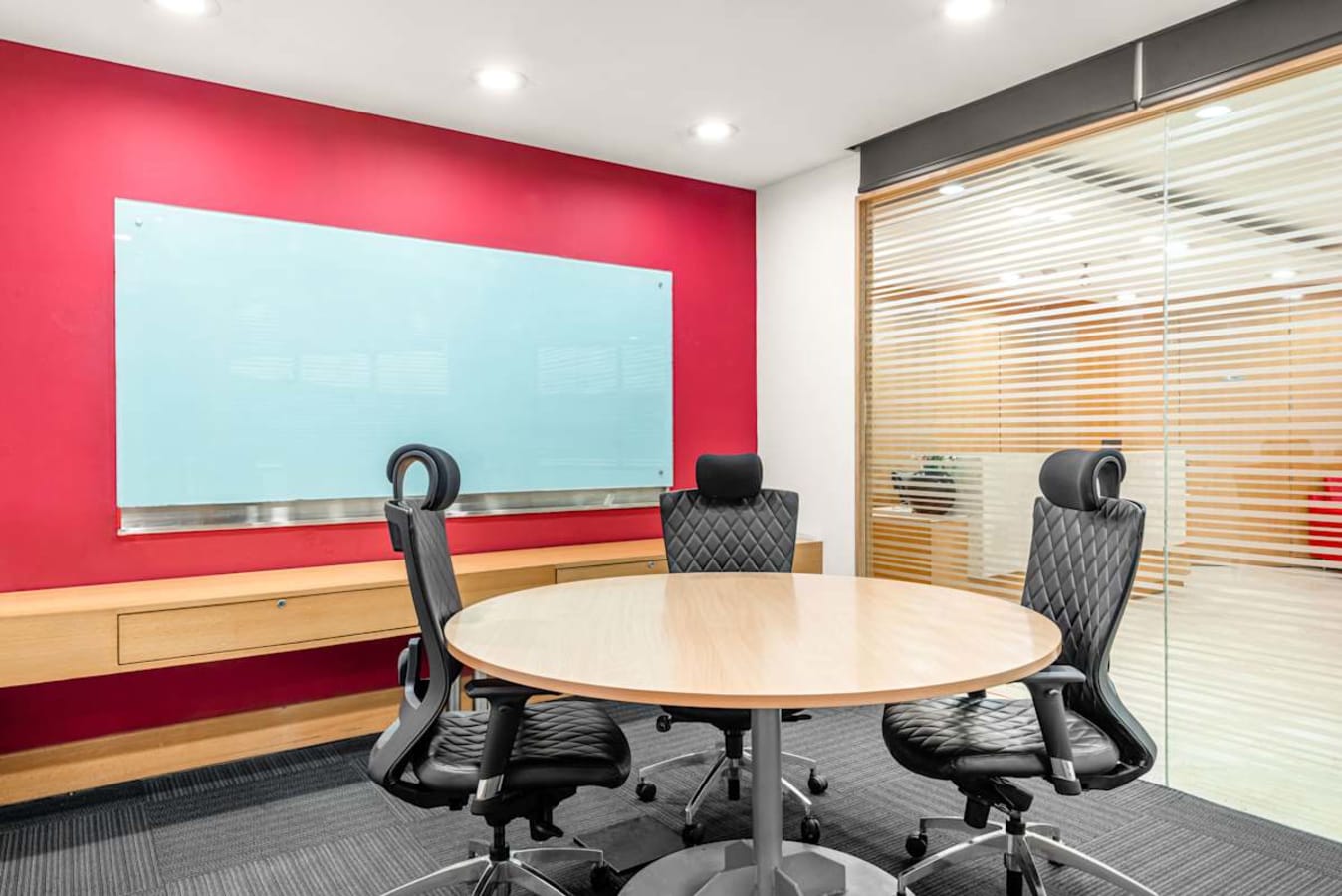 Modern meeting room with ergonomic chairs, vibrant red accent wall, and a large glass board.