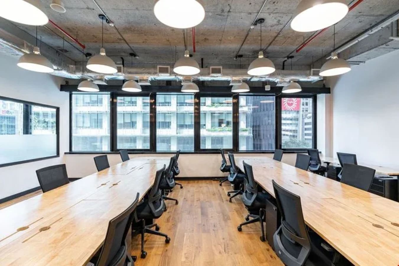 Modern coworking space with large wooden desks, ergonomic chairs, and ample natural light.