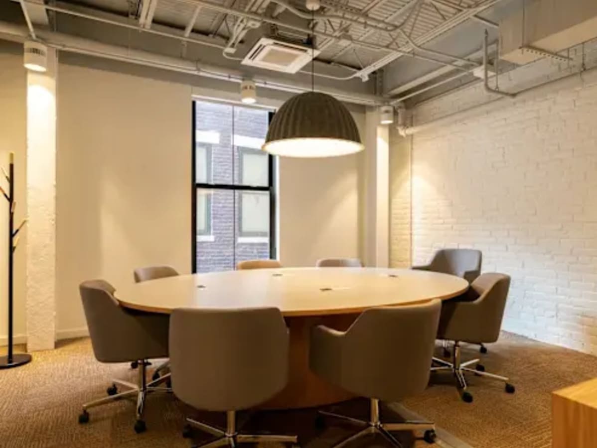 Modern coworking space with a spacious round table, ergonomic chairs, and ample natural lighting.