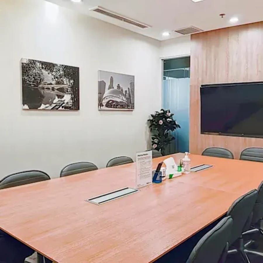 Modern conference room with large wooden table, ergonomic chairs, and wall-mounted TV. Ideal for meetings.