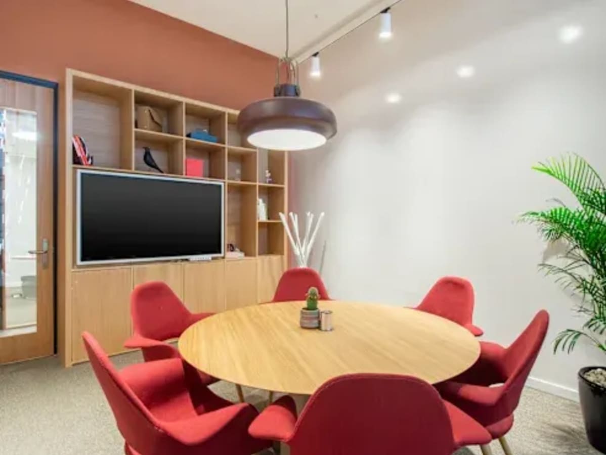 Modern coworking area with a round table, red chairs, ample shelving, and accent lighting.