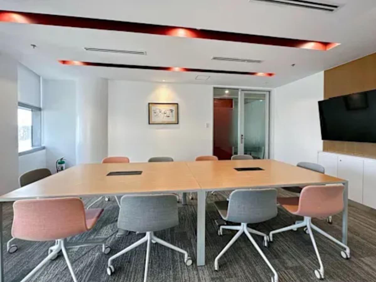 Modern coworking space with large meeting table, ergonomic chairs, and ample natural light.