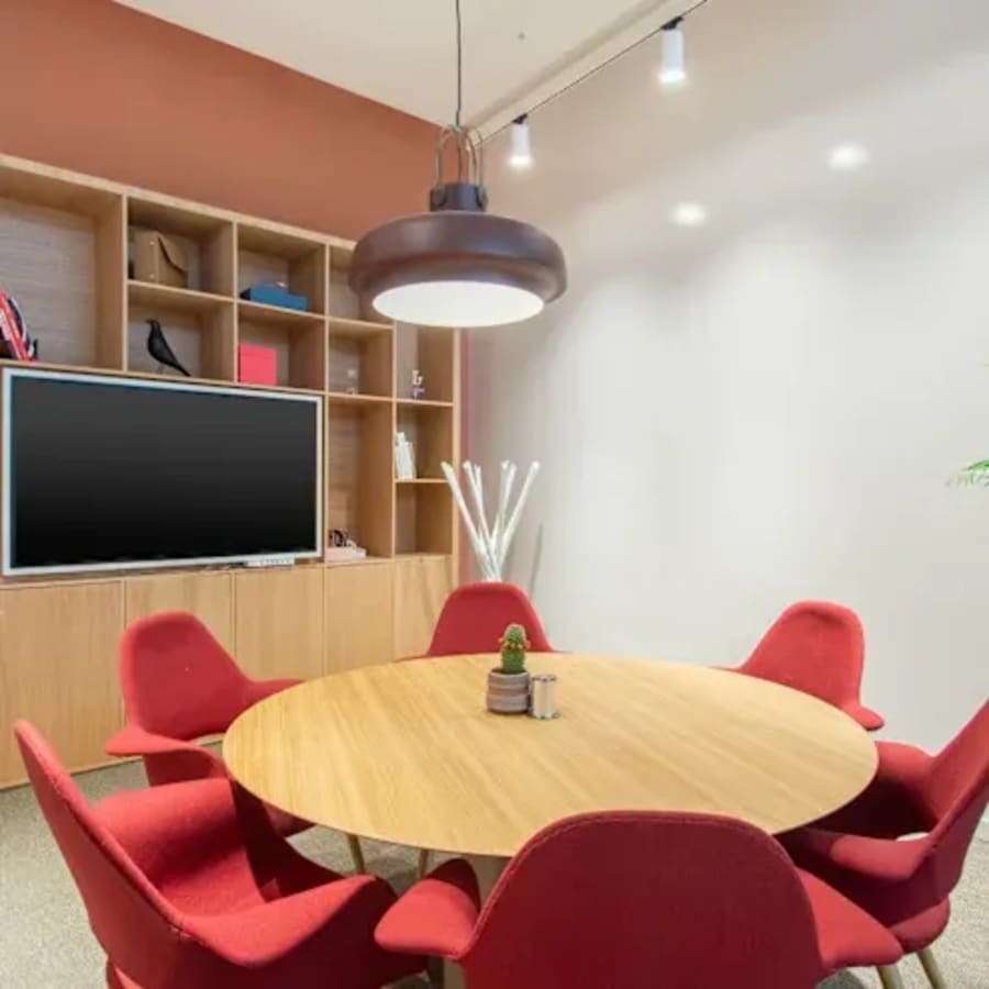 Modern coworking meeting area with vibrant red seating and advanced presentation screen.
