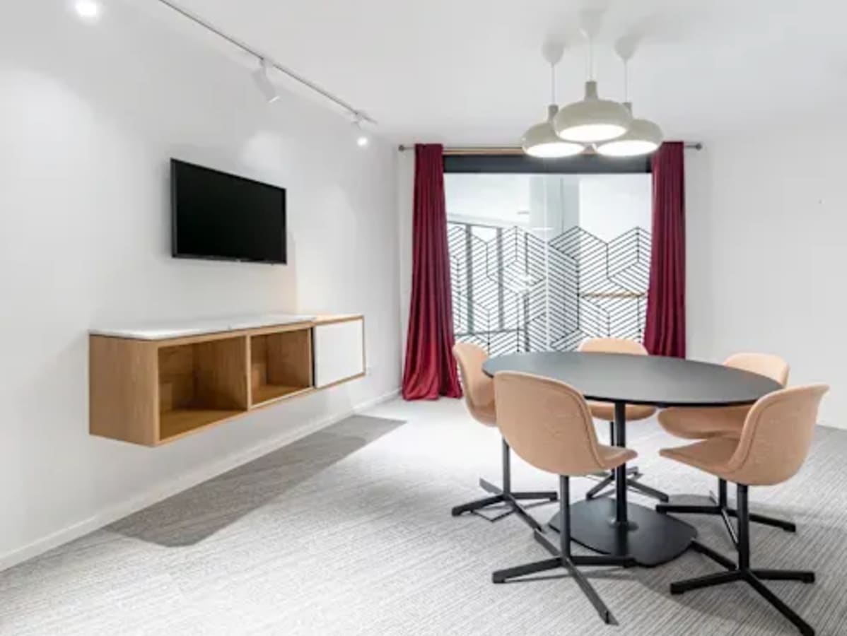 Modern coworking space with a sleek meeting area, featuring stylish chairs, a round table, and wall-mounted TV.