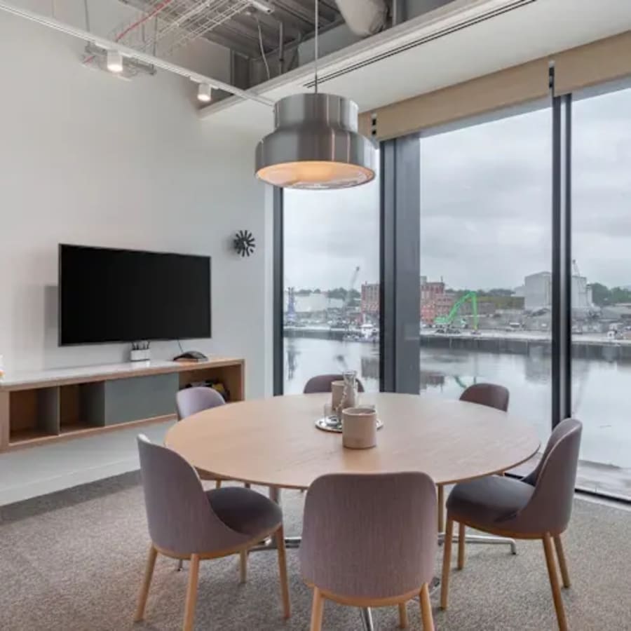Modern coworking space with round table, waterfront views, and natural light. Perfect for meetings.