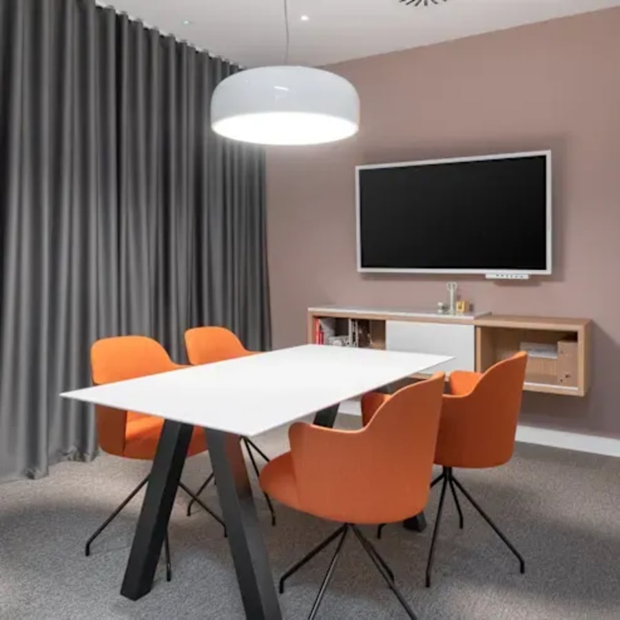 Modern meeting area with sleek table, vibrant orange chairs, and a large screen for presentations.