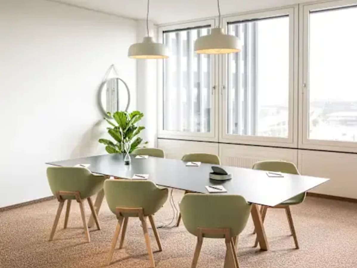Modern coworking space with natural light, sleek table, and stylish seating for collaboration.