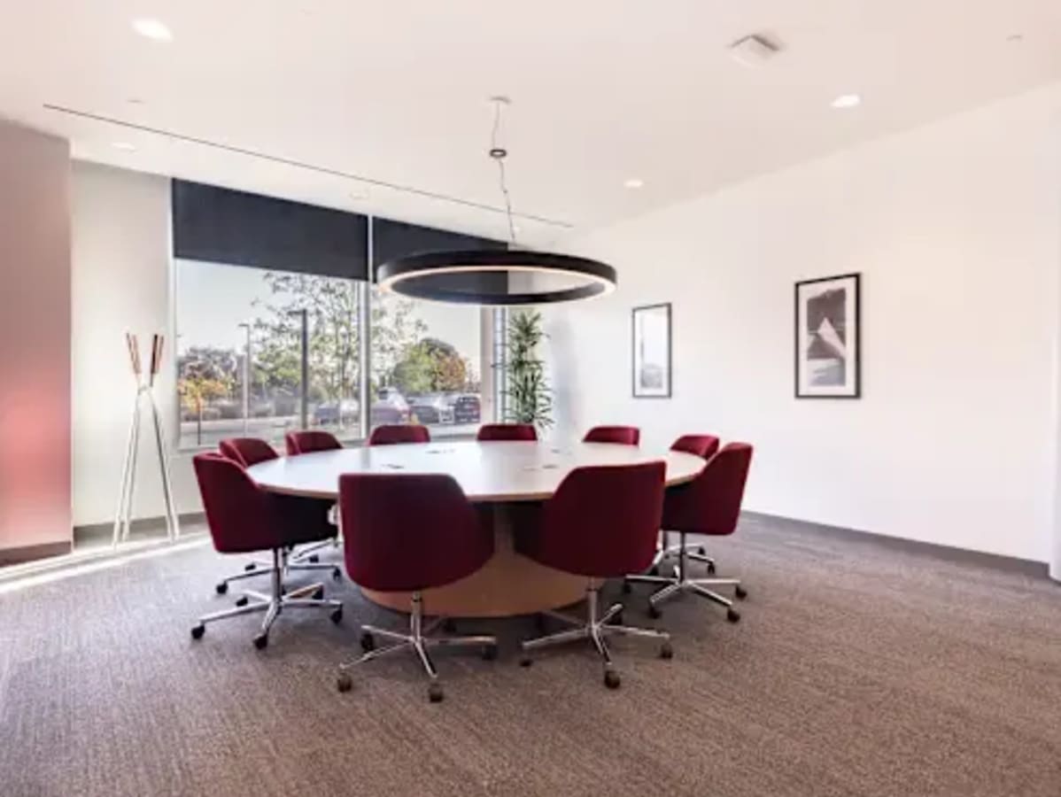 Modern meeting room with large round table, plush red chairs, and ample natural light.