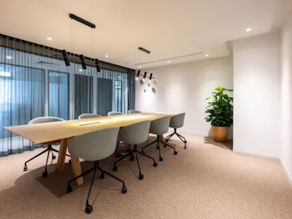 Modern coworking space with a large conference table, stylish chairs, and abundant natural light.