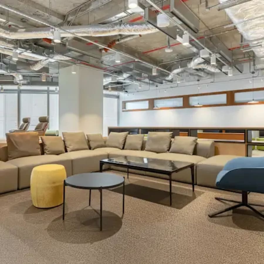 Modern coworking lounge with ample seating, sleek tables, and industrial ceiling design.