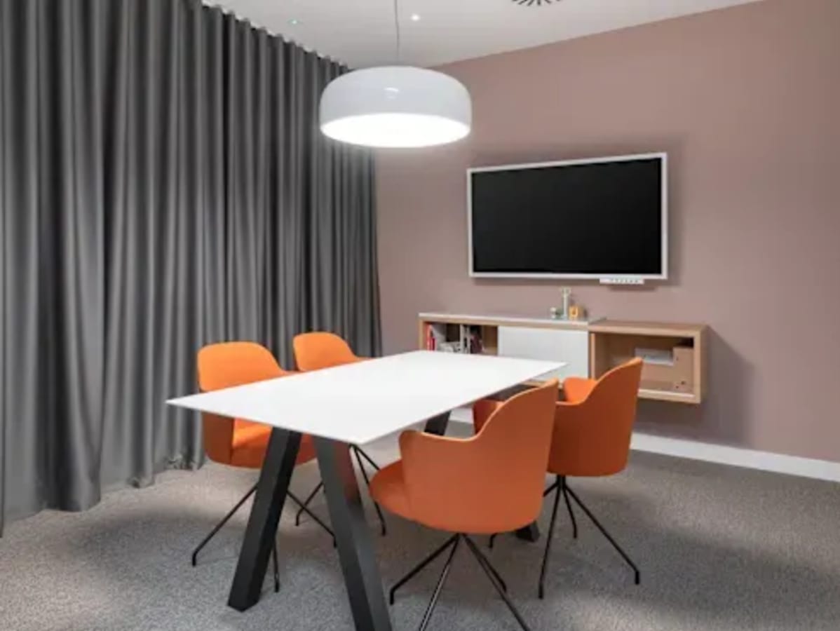 Modern meeting area with sleek table, vibrant chairs, and a wall-mounted TV, ideal for collaboration.