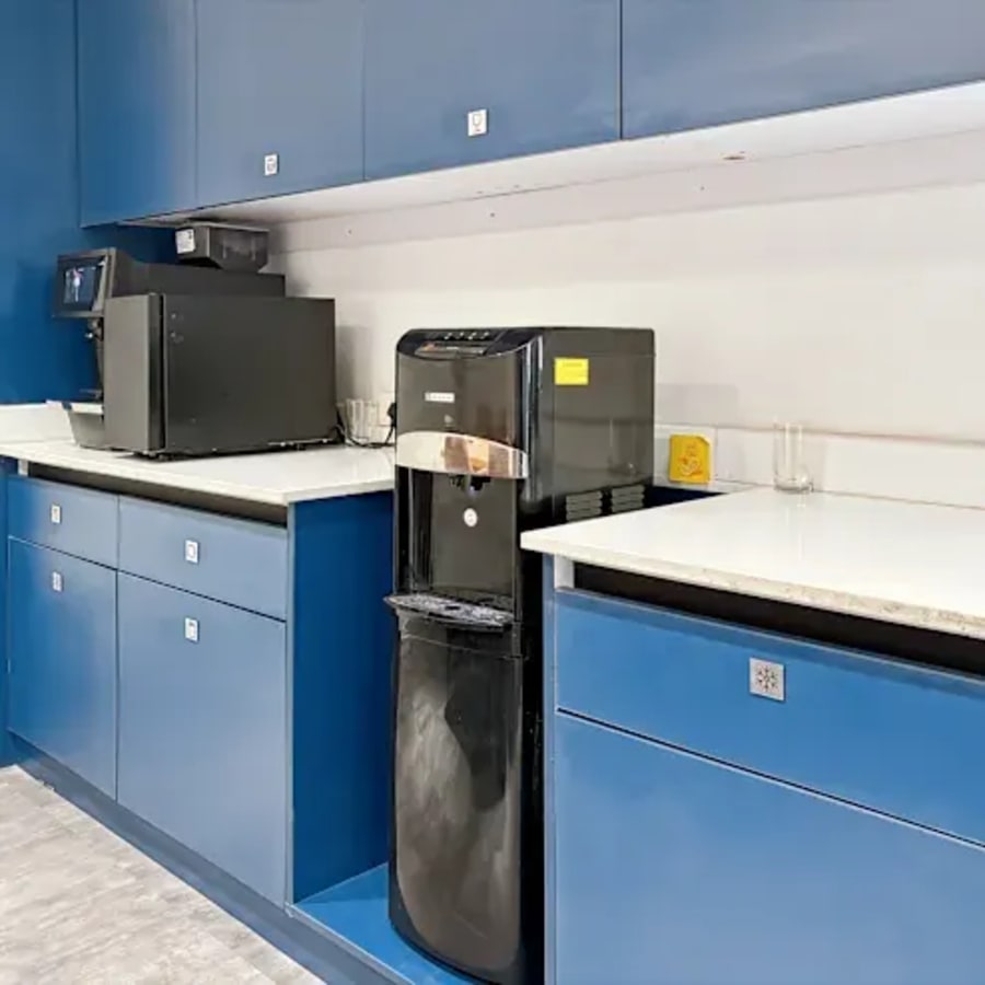 Modern kitchenette with sleek blue cabinetry and essential appliances for convenient office breaks.