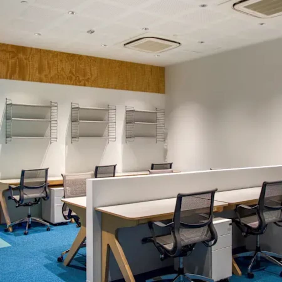 Modern coworking area with sleek desks, ergonomic chairs, and ample shelving. Perfect for productivity.