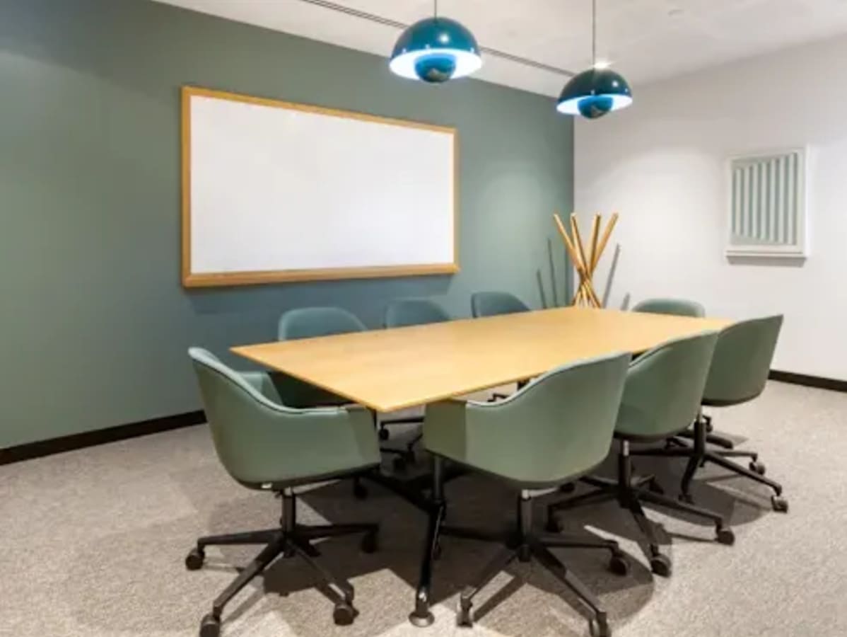 Modern meeting room with ample seating, stylish lighting, and a large whiteboard.