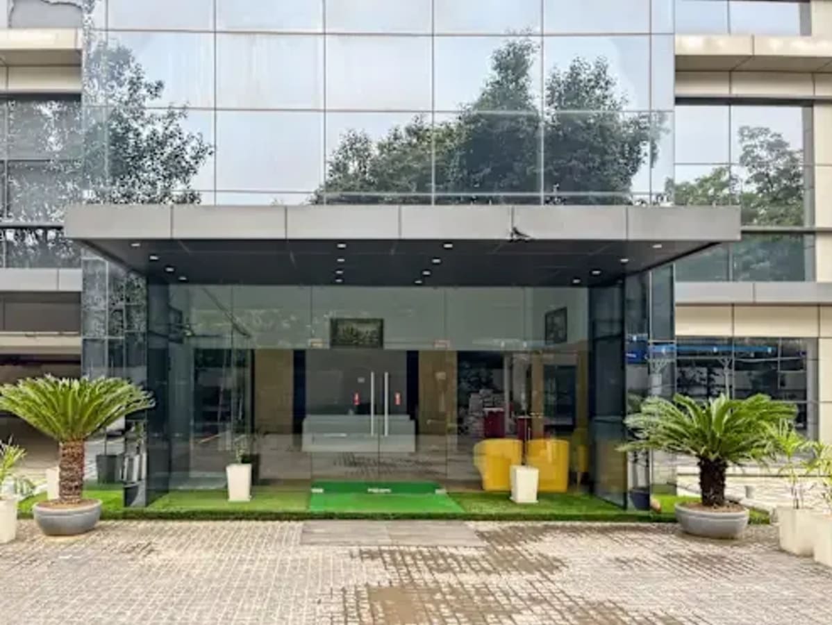 Sleek entrance to a modern coworking space in Gali Number 4, featuring glass facade and greenery.