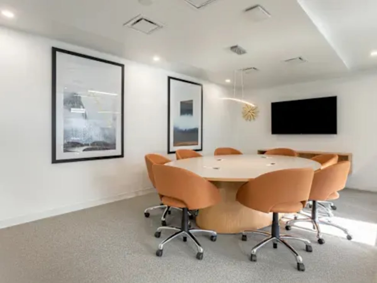 Modern meeting room with a round table, cozy chairs, and a large screen for presentations.