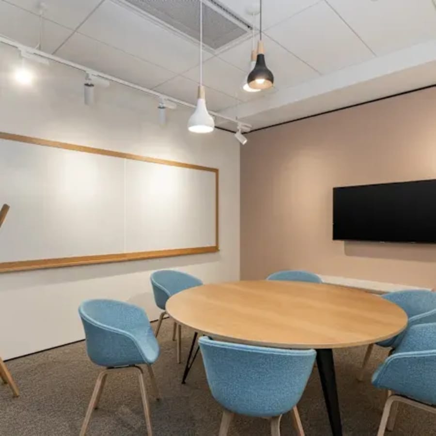 Modern conference area with round table, plush blue chairs, and a wall-mounted TV for presentations.