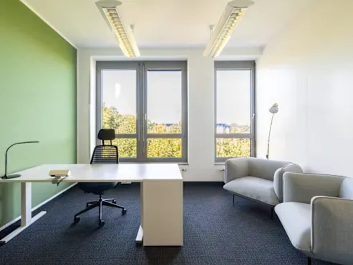 Modern coworking space with natural light, contemporary furniture, and a serene green accent wall.