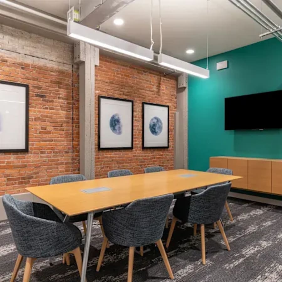 Sleek coworking space featuring a modern meeting room with exposed brick, stylish seating, and ample lighting.