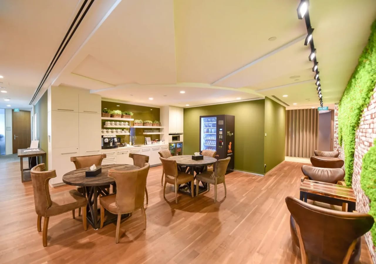 Modern coworking lounge with sleek tables, vibrant greenery, and convenient amenities.