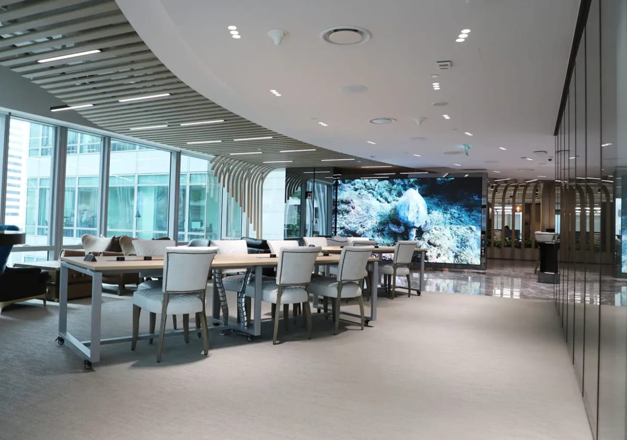 Modern coworking space with sleek design, ample natural light, and large presentation screen.