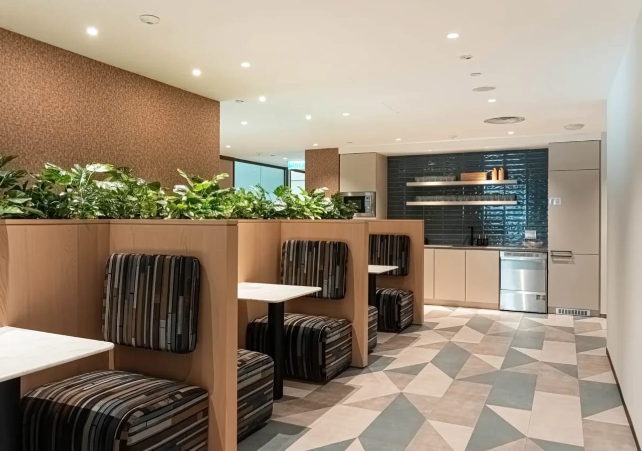 Stylish coworking booths with greenery and kitchen amenities for a productive workspace.