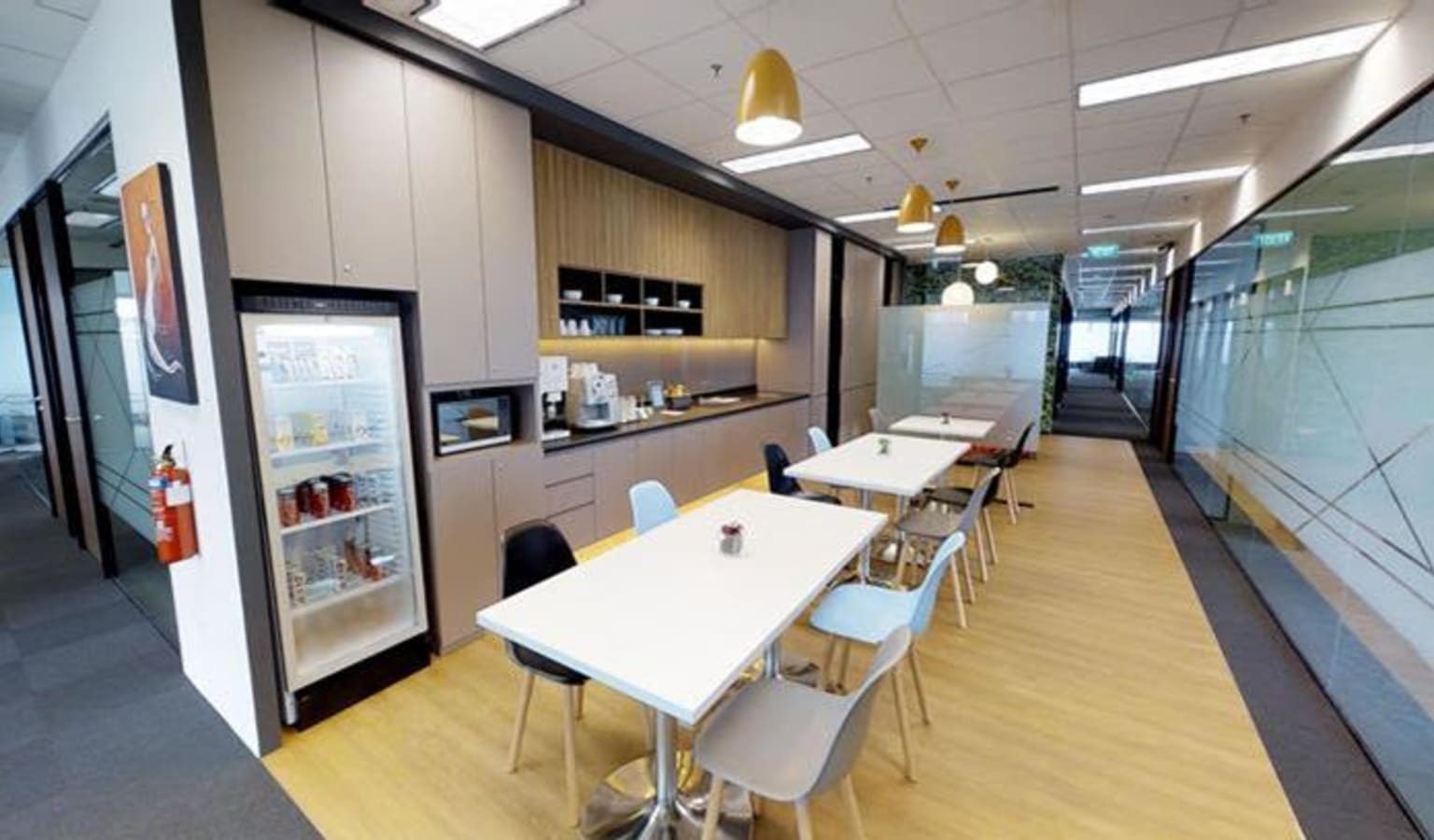 Modern coworking area with sleek tables, vibrant chairs, and a well-equipped kitchenette.