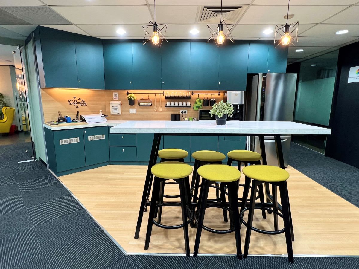 Modern coworking kitchen with sleek teal cabinetry, island seating, and stylish lighting.