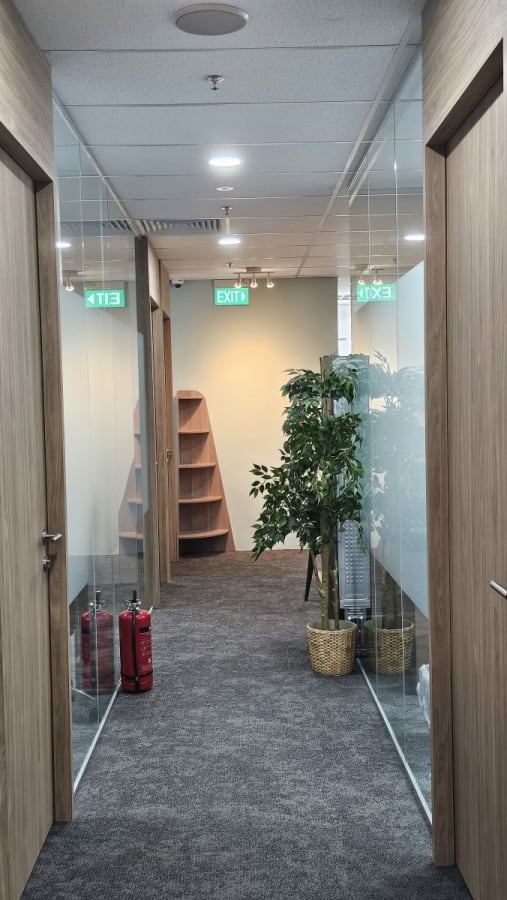 Modern coworking corridor with glass partitions, bright lighting, and lush greenery.