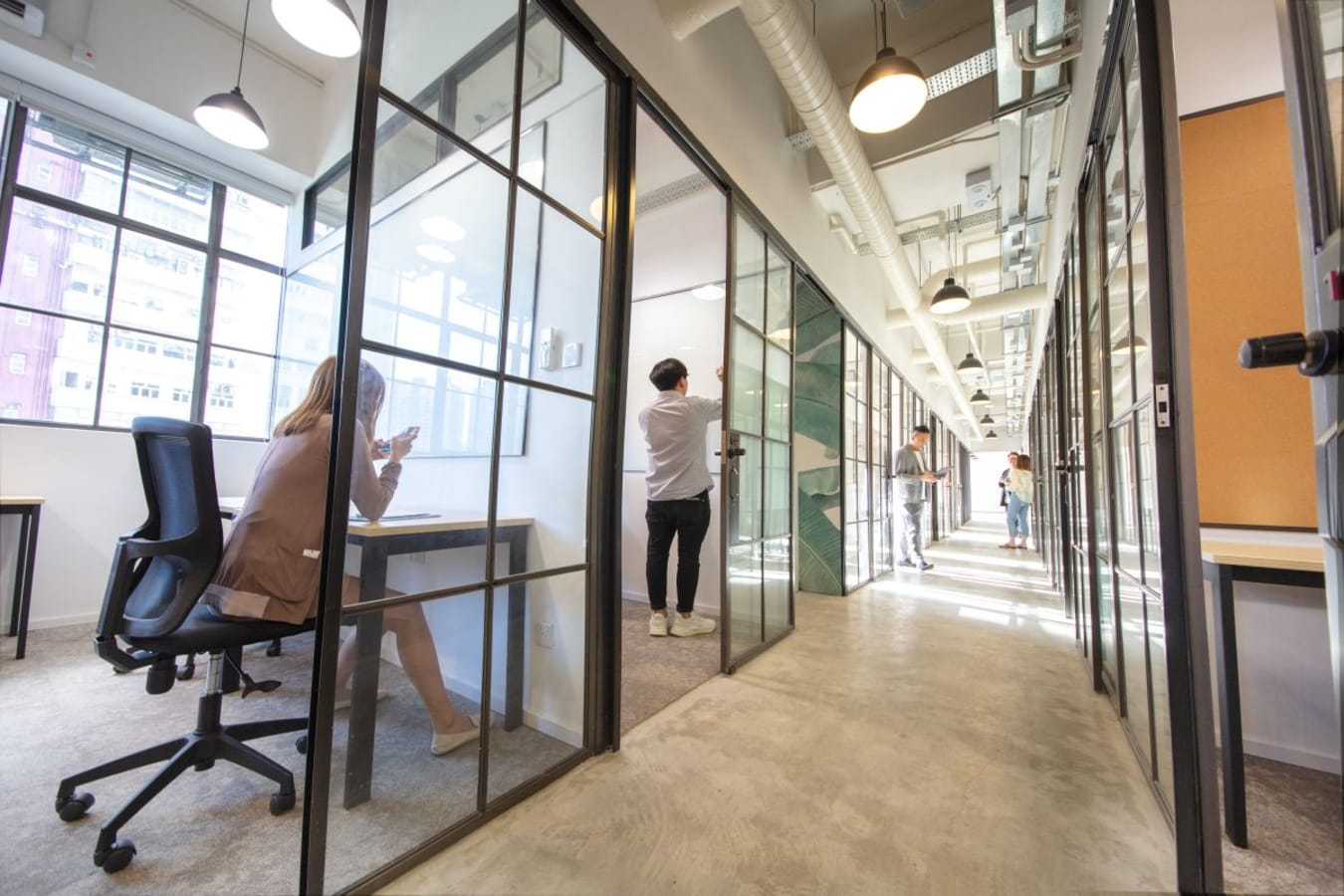 Modern coworking space with private glass offices, abundant natural light, and a collaborative atmosphere.