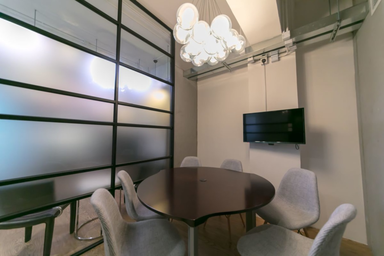 Modern meeting space with sleek table, cozy chairs, frosted glass panels, and overhead lighting.