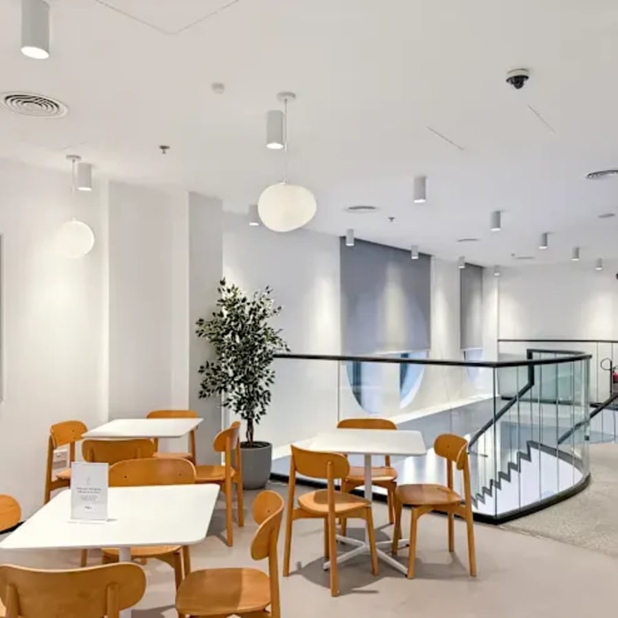 Bright coworking space with modern seating, natural light, and a sleek staircase. Perfect for collaboration.